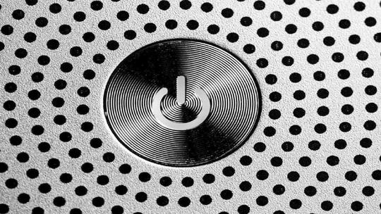 Close-up of a power button surrounded by a pattern of small black dots on a metallic surface.