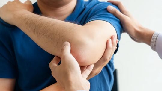 A person in a blue shirt having their elbow examined by a healthcare professional.