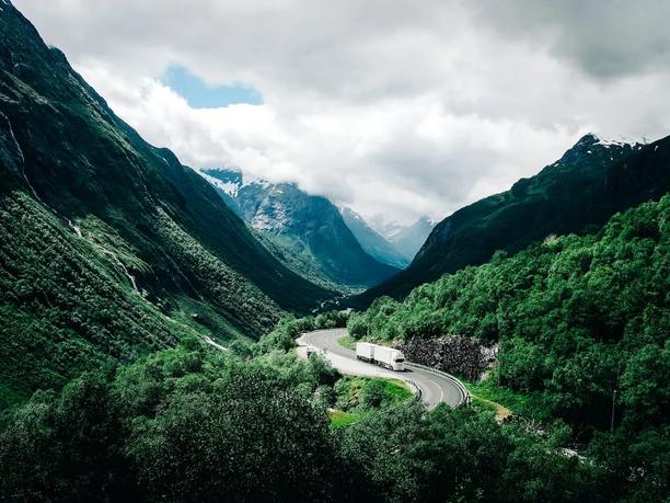 A white truck driving on a winding road through a lush green valley.