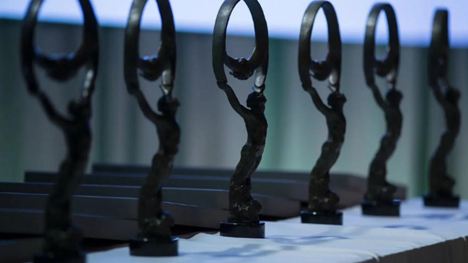 A row of elegant bronze statues on a table, each depicting a figure holding a circular shape above their head, set against a softly lit background.