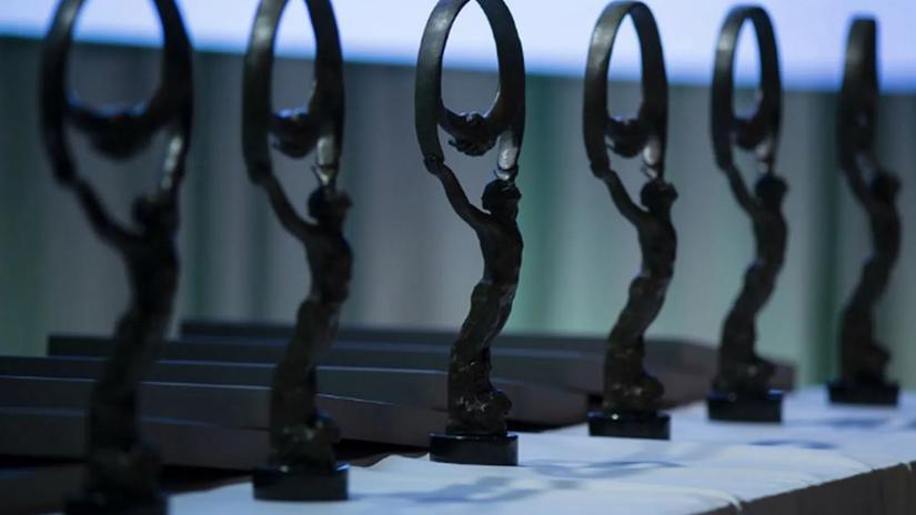 A row of elegant bronze statues on a table, each depicting a figure holding a circular shape above their head, set against a softly lit background.