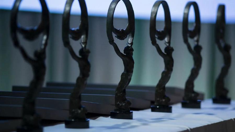 A row of elegant bronze statues on a table, each depicting a figure holding a circular shape above their head, set against a softly lit background.