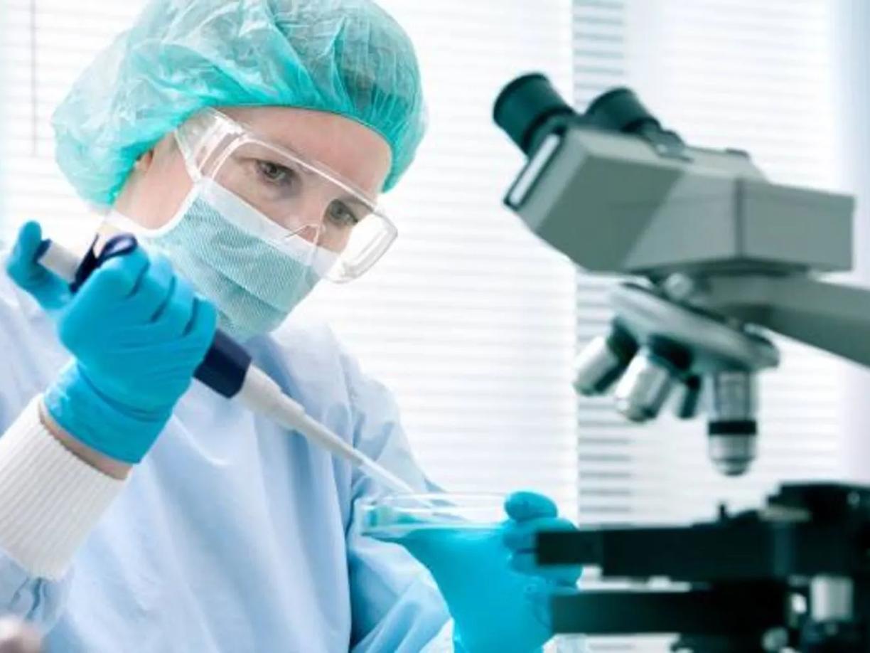 A scientist wearing protective gear with a microscope nearby.