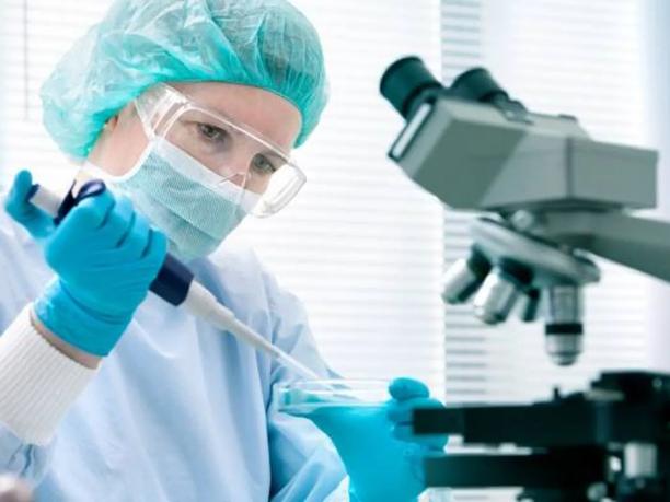 A scientist wearing protective gear with a microscope nearby.