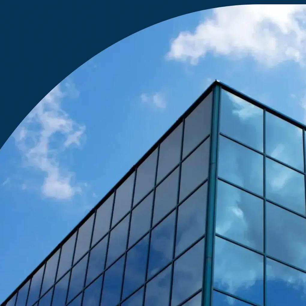 A modern glass building corner reflecting the sky and clouds, with a dark blue curved overlay at the top.