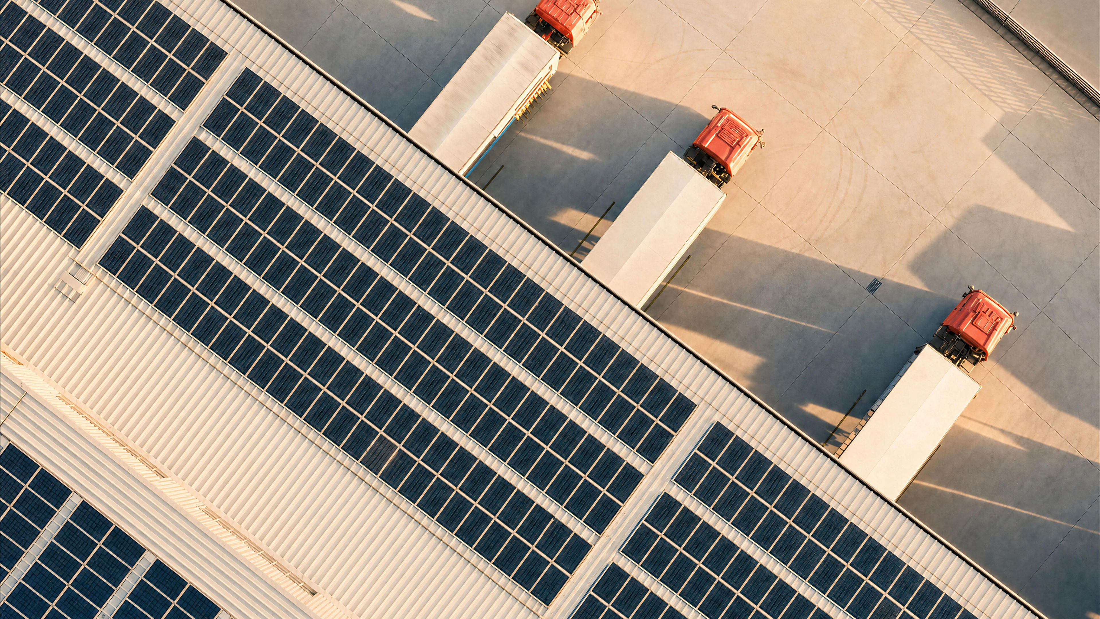 Warehouse with solar panels on the roof and three trucks.