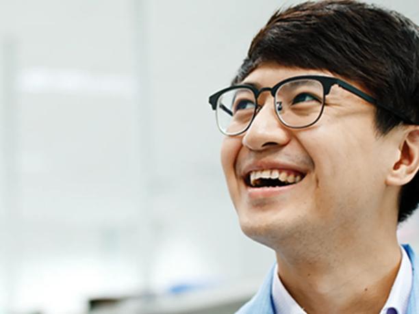 A smiling man wearing glasses and a light blue shirt.