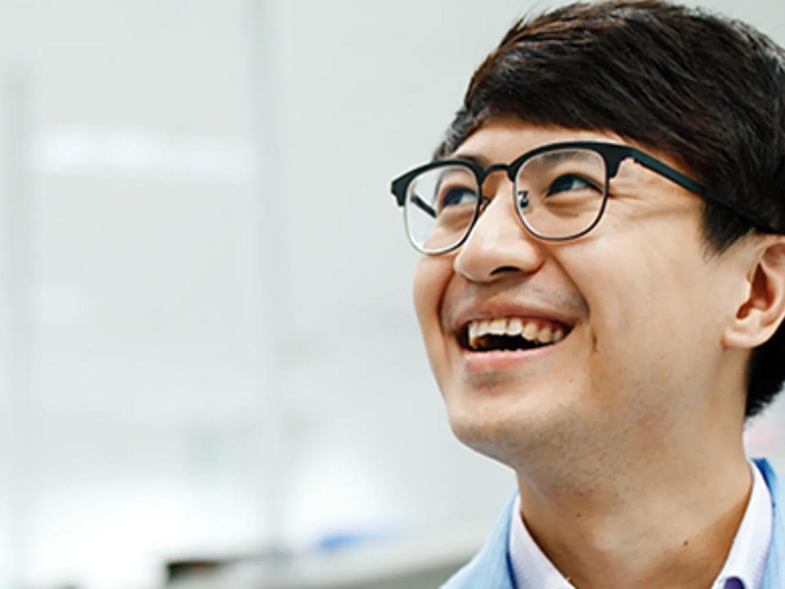 A smiling man wearing glasses and a light blue shirt.