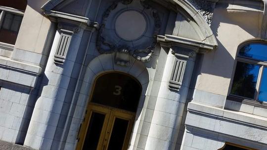 A close-up view of an ornate stone building entrance with classical architectural details, including columns and decorative moldings, featuring a large arched doorway with the number 3 above it.