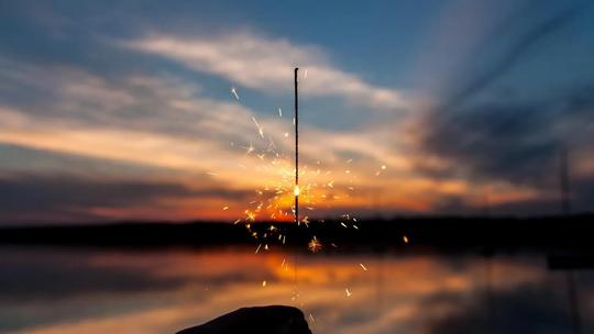 picture of a lit sparkler in front of a lake at sunset