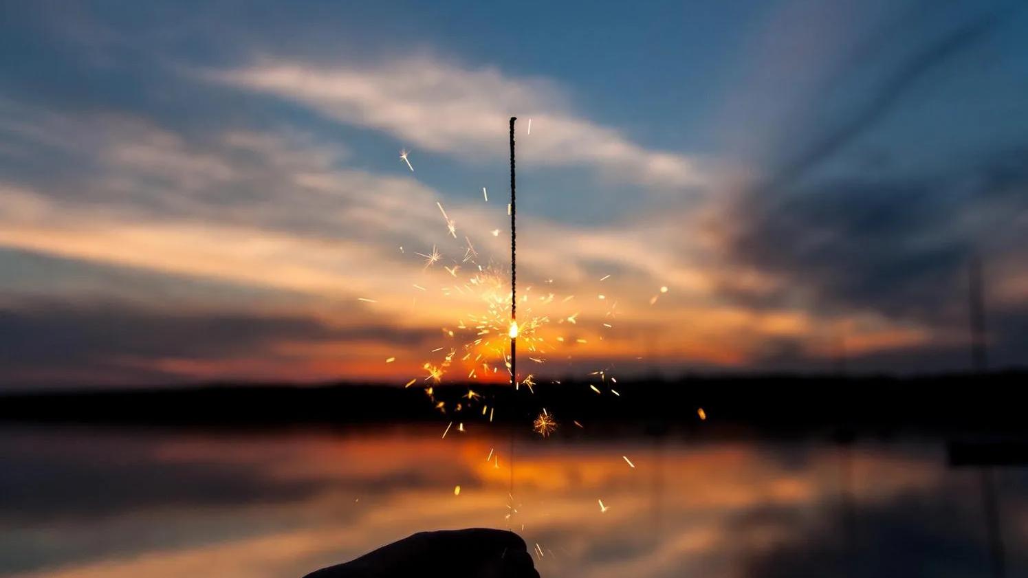 picture of a lit sparkler in front of a lake at sunset