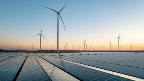 Solar panels in the foreground with multiple wind turbines stretching into the distance at sunset.