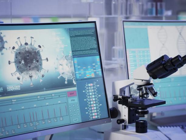 A laboratory setup with a microscope next to a computer screen displaying a digital image of a virus and DNA sequences.