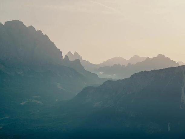 A serene mountain landscape at dusk, with layers of misty peaks fading into the distance under a soft, pale sky.