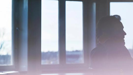 Silhouette of a person sitting in front of large windows with a soft, blurred foreground.