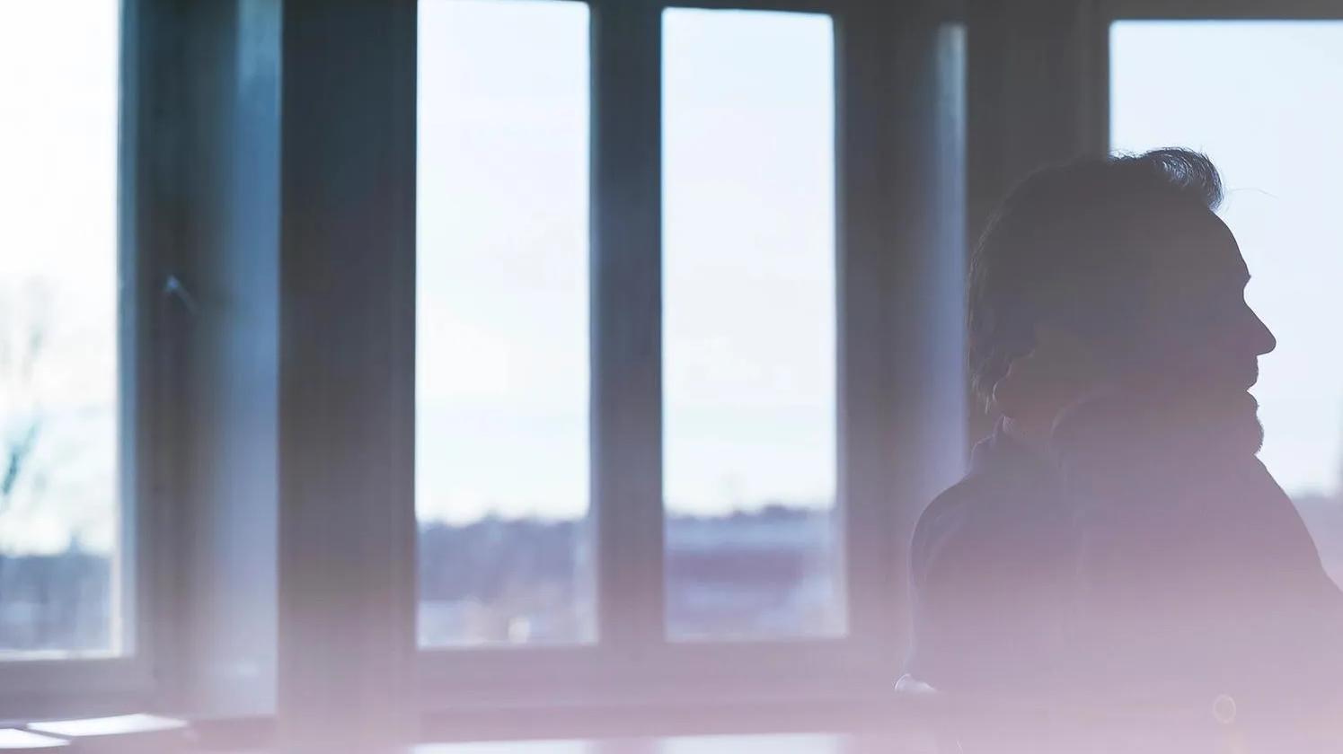 Silhouette of a person sitting in front of large windows with a soft, blurred foreground.