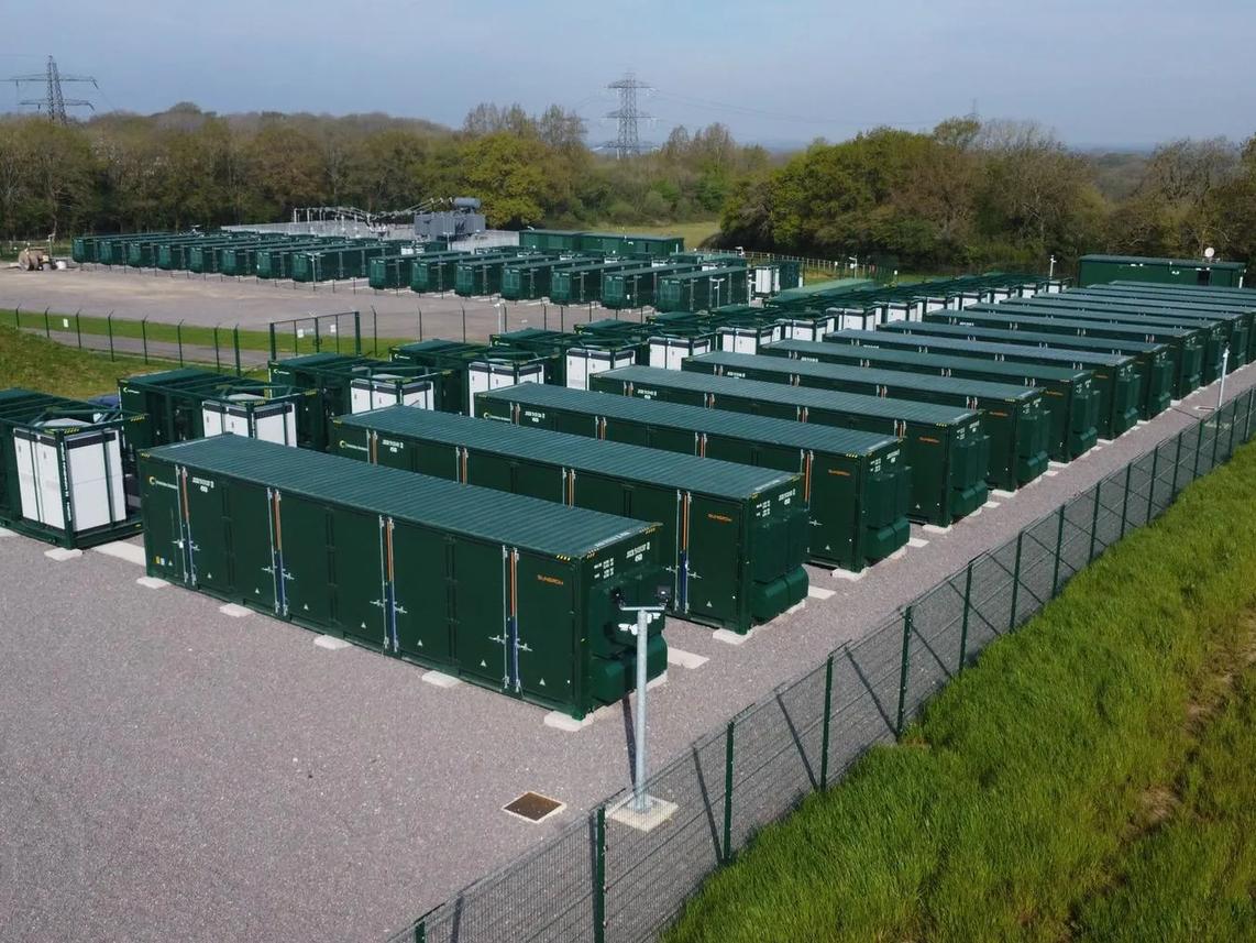 Aerial view of a large battery storage facility with multiple green containers arranged in rows.