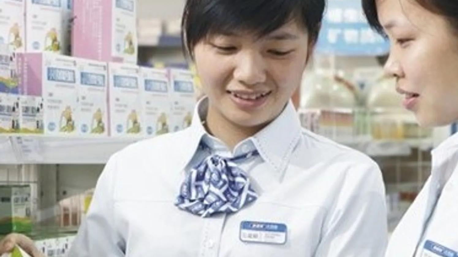 Two employees in a store discussing a product, with shelves of boxed items in the background