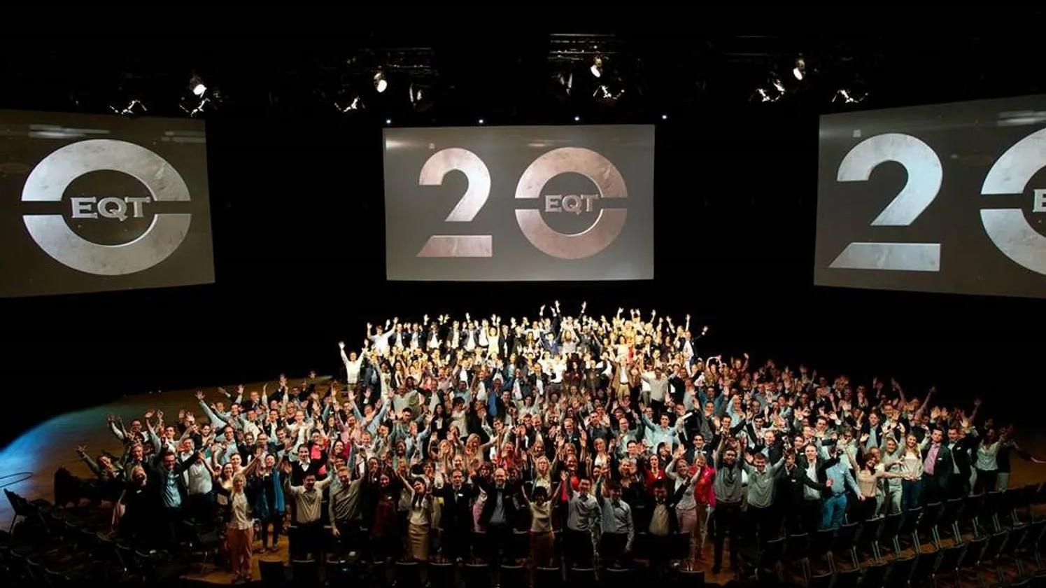 A large group of people celebrating in an auditorium with two screens displaying the EQT logo and the number 20, indicating an anniversary or milestone event.'
