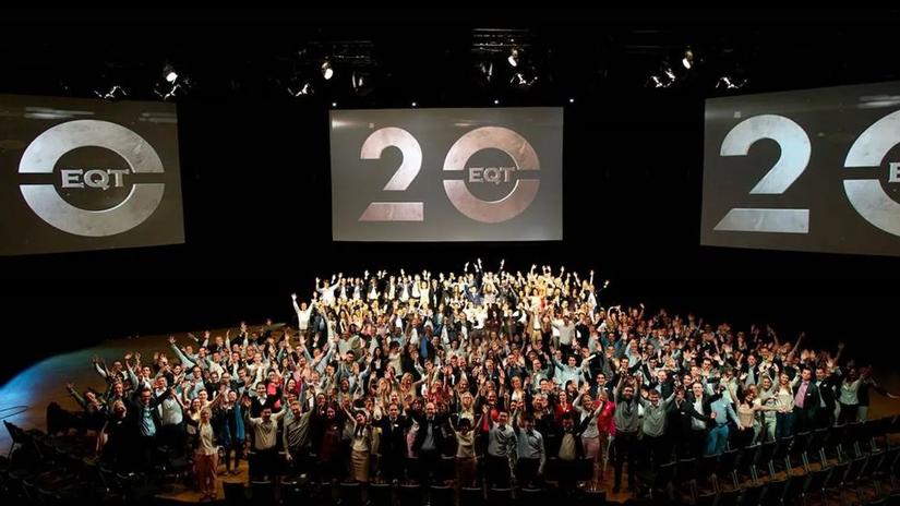 A large group of people celebrating in an auditorium with two screens displaying the EQT logo and the number 20, indicating an anniversary or milestone event.'
