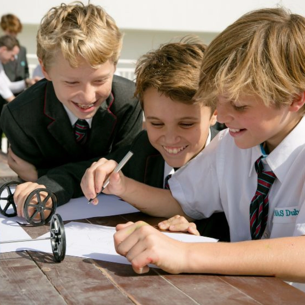Three children smiling and writing on a school project.