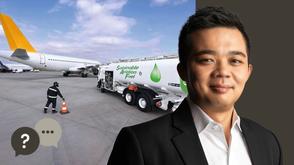 Man in a black suit with a airport and a plane in the background with a fuel tank.