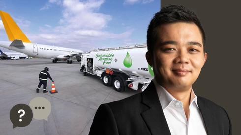 Man in a black suit with a airport and a plane in the background with a fuel tank.