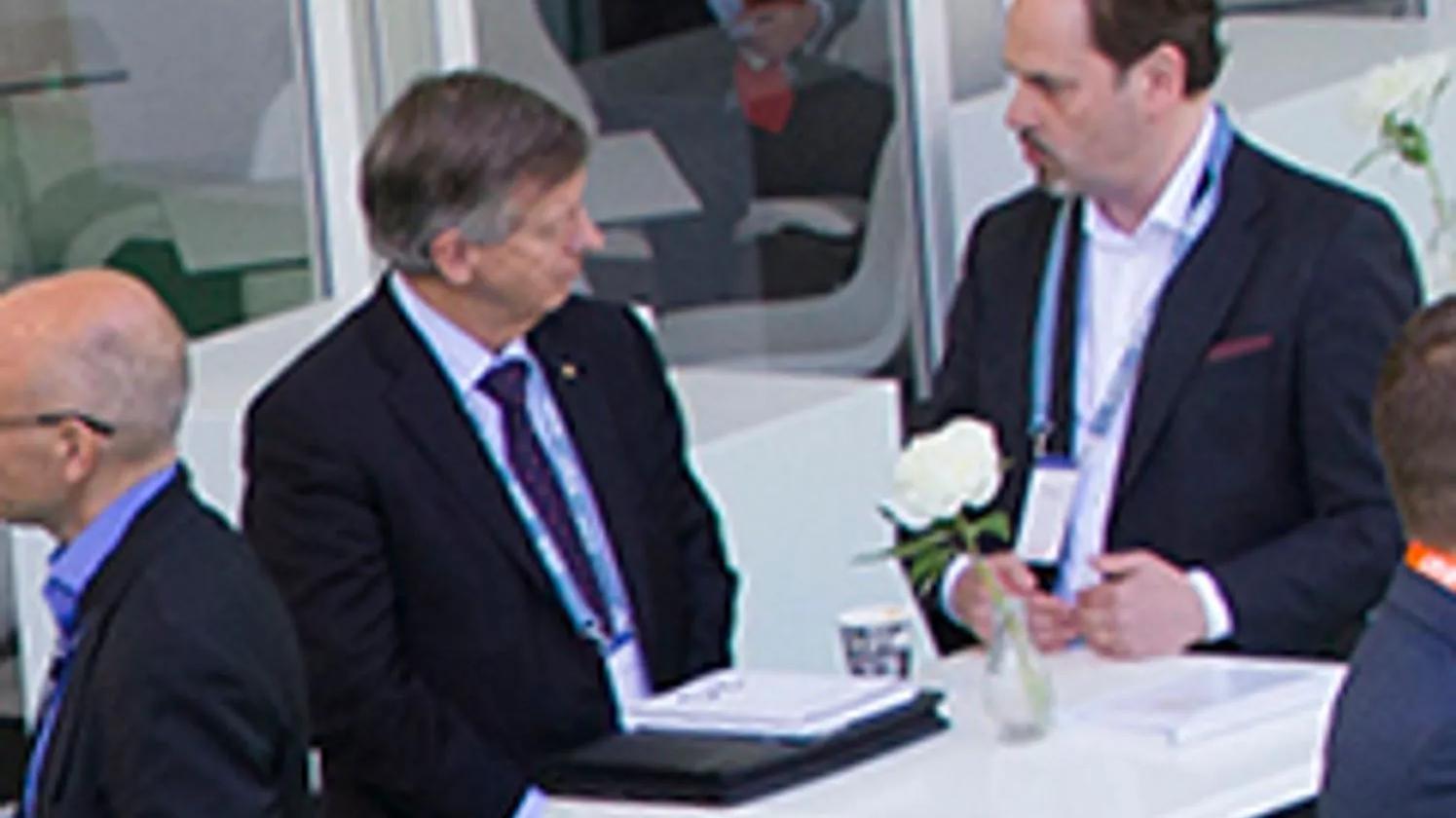 Two men in suits having a conversation at a small table in a modern office setting.