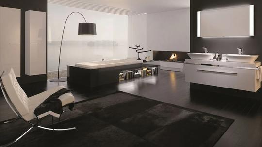 A modern, luxurious bathroom with a sleek black and white design, featuring a large bathtub, double sinks, a fireplace, and a contemporary chair.