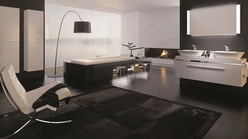 A modern, luxurious bathroom with a sleek black and white design, featuring a large bathtub, double sinks, a fireplace, and a contemporary chair.