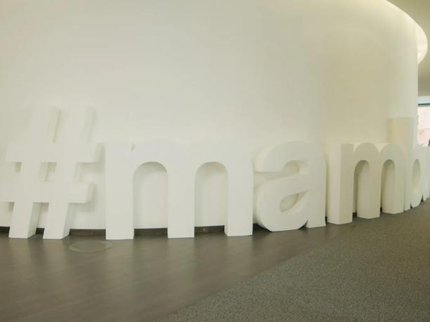 Large white 3D letters spelling "#mambo" are arranged along a curved wall in an office space.