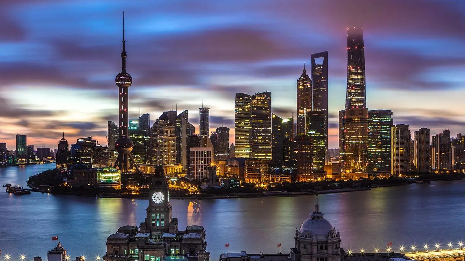 Skyline of Shanghai at dusk, featuring the Oriental Pearl Tower and modern skyscrapers reflecting on the Huangpu River.