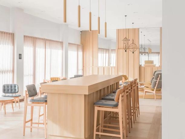 A modern, minimalist dining area with a long wooden table surrounded by high chairs.