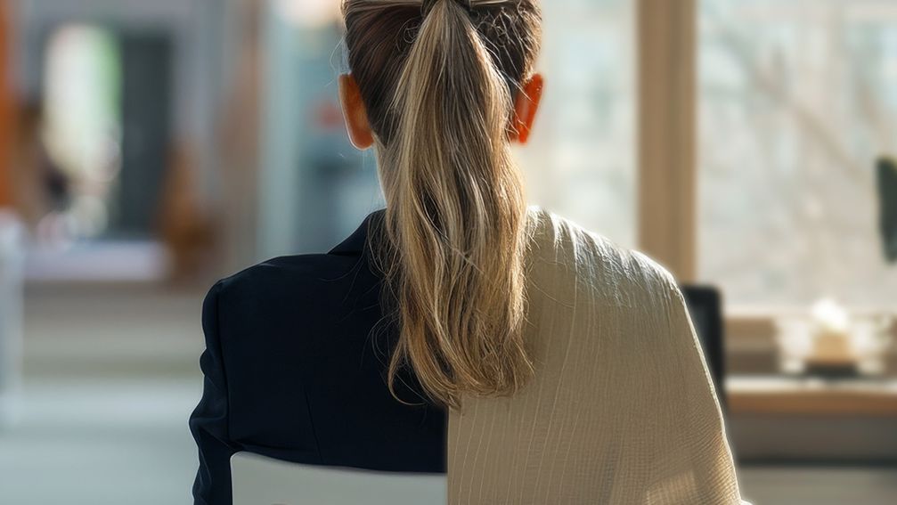 A woman sits at a desk, looking away from the viewer.