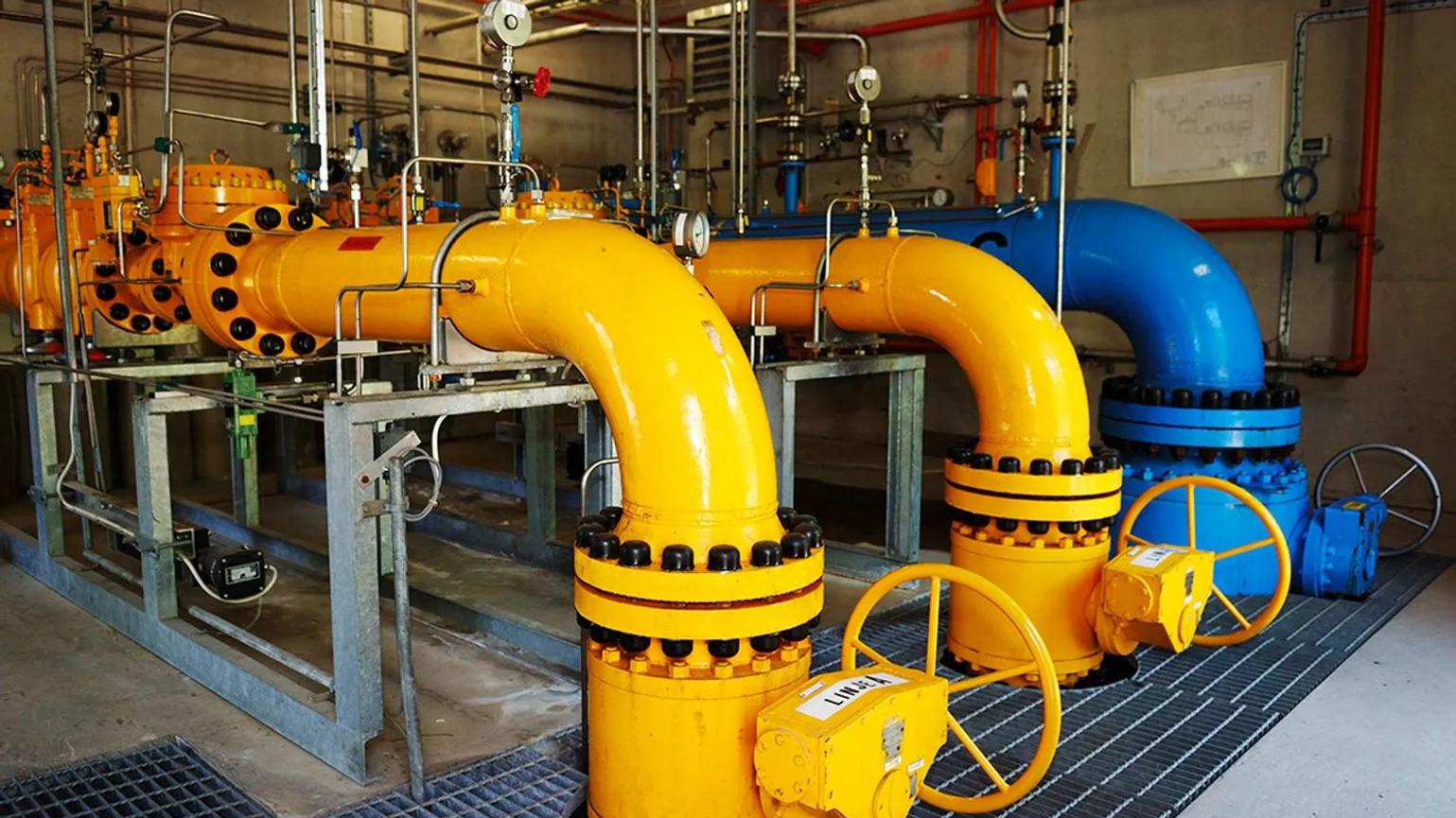 Industrial facility with large yellow and blue pipes, featuring valves and gauges, used for controlling the flow of liquids or gases.