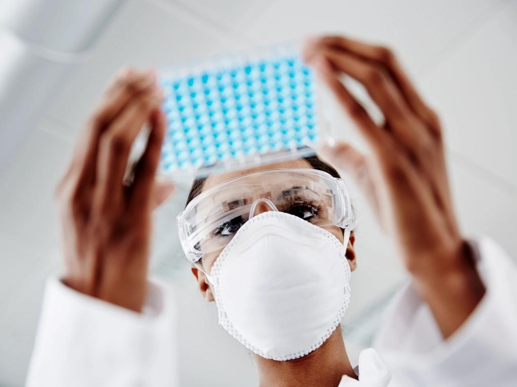 Close-up of two gloved hands adjusting a microscope