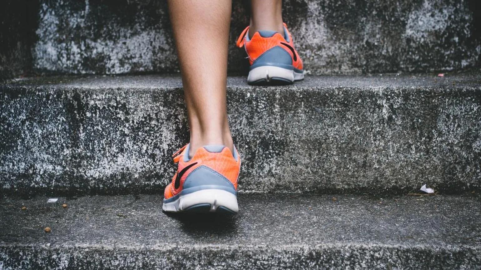 Close-up of a person wearing orange and gray running shoes, walking up concrete steps.