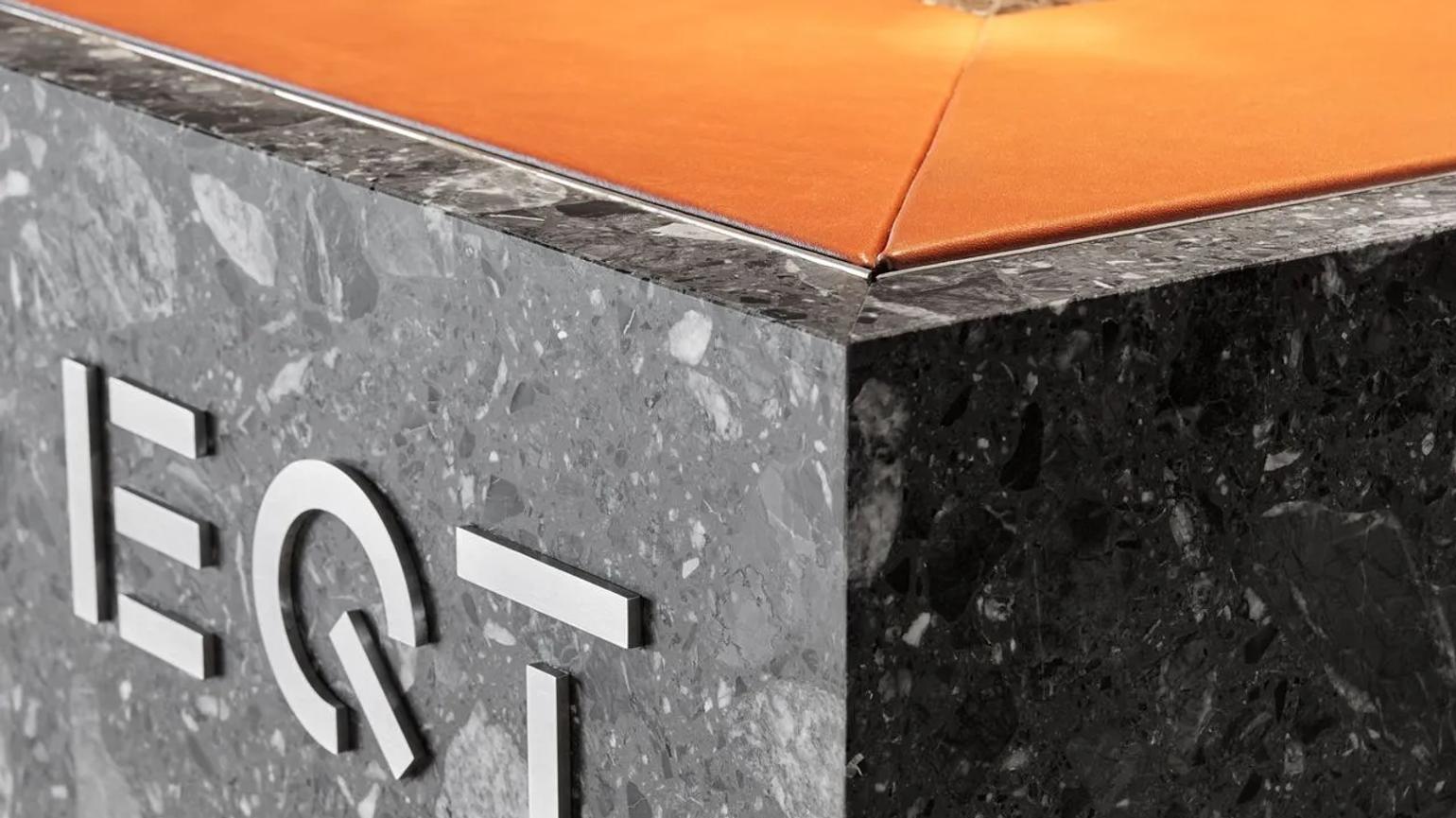 Close-up of a marble reception desk with the EQT logo in white, featuring an orange leather top.