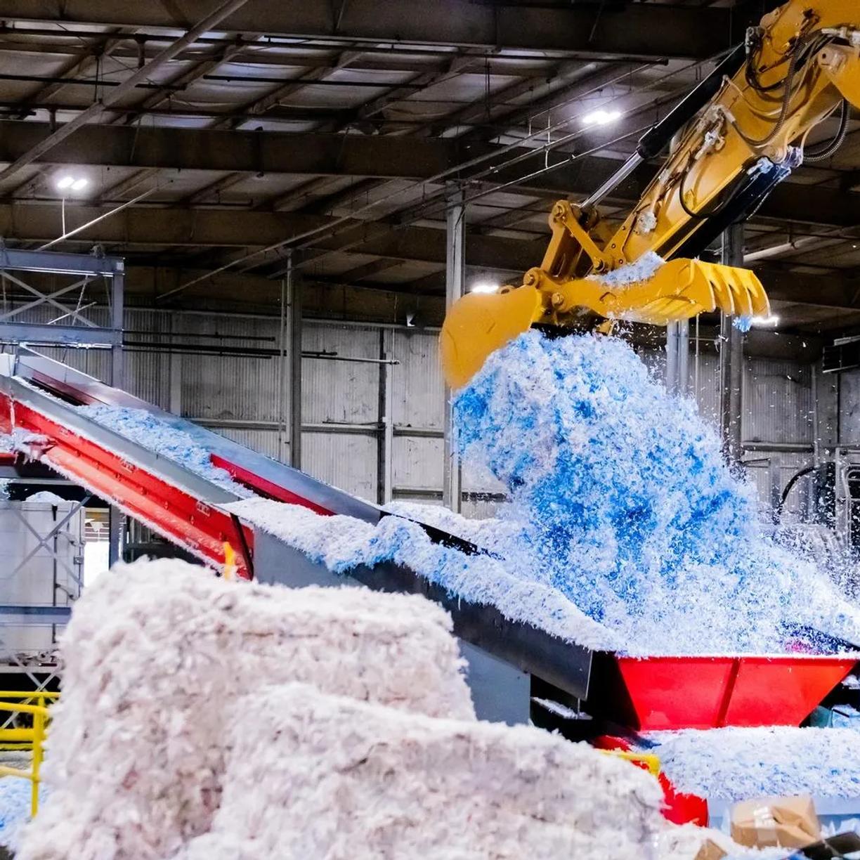 A large industrial machine processing shredded blue and white material.
