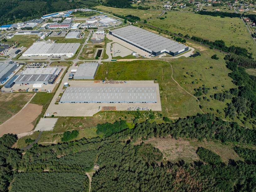 A closer aerial view of several large warehouse buildings and industrial facilities, bordered by open fields and forested areas.