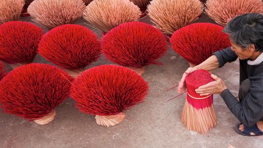 A person arranging bundles of red incense sticks, with multiple bundles spread out on the ground.