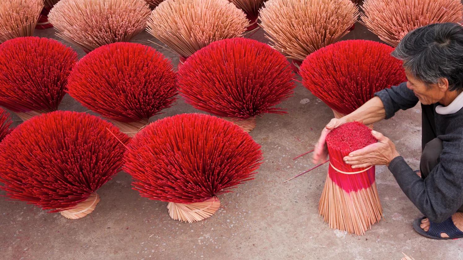 A person arranging bundles of red incense sticks, with multiple bundles spread out on the ground.