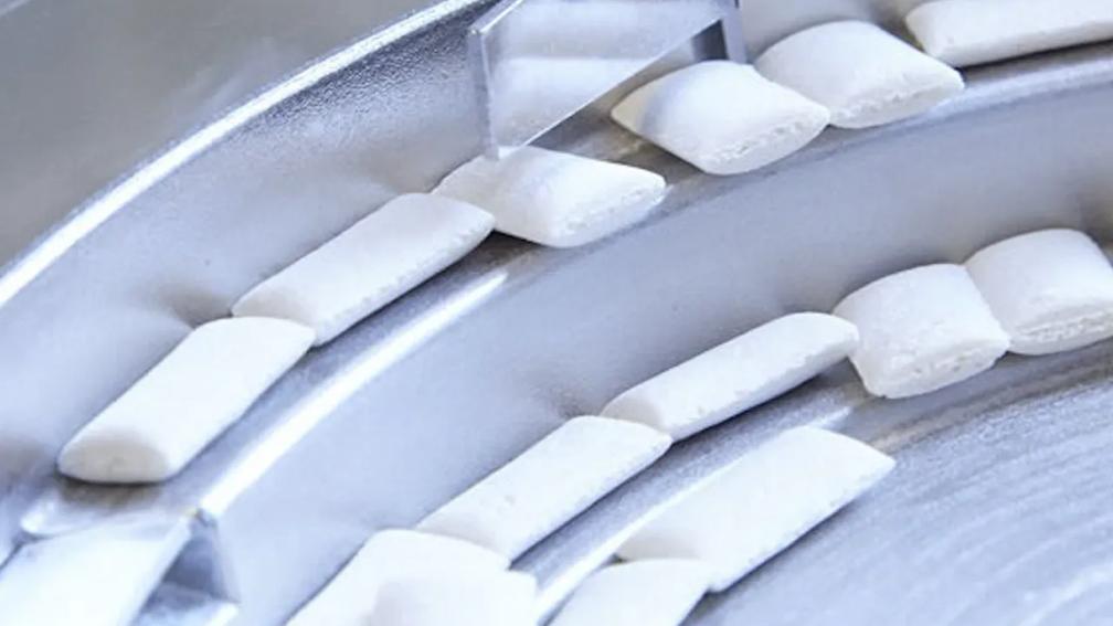 Close-up of white pieces on a metal conveyor belt.