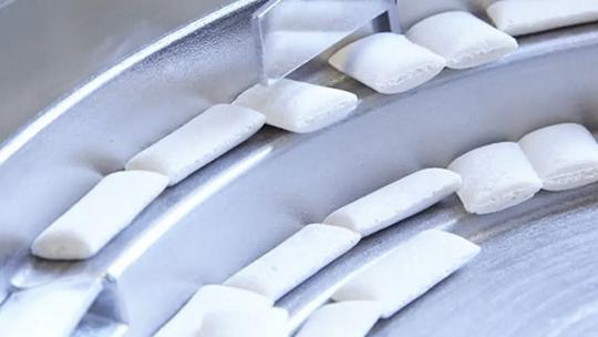 Close-up of white pieces on a metal conveyor belt.