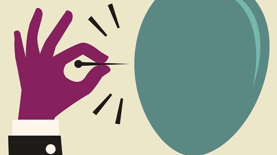 A hand holds a pin that's about to pop a balloon.