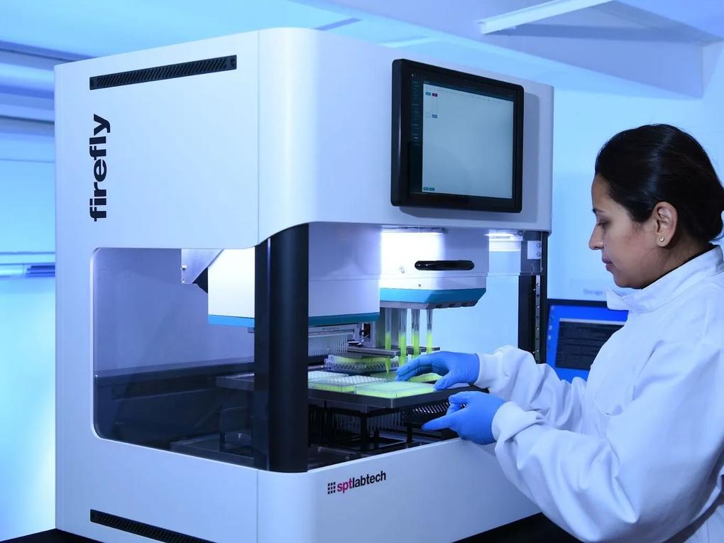 A scientist wearing gloves operates a automated laboratory machine.