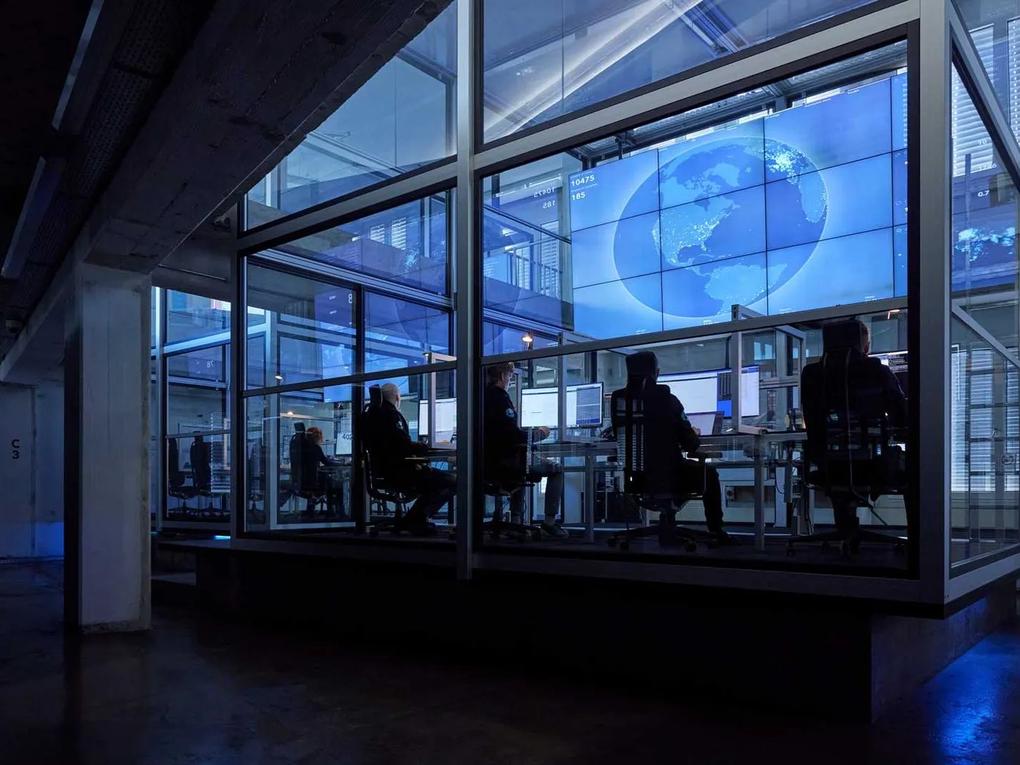 A high-tech control room with people working at desks, surrounded by large screens displaying a digital globe and data.