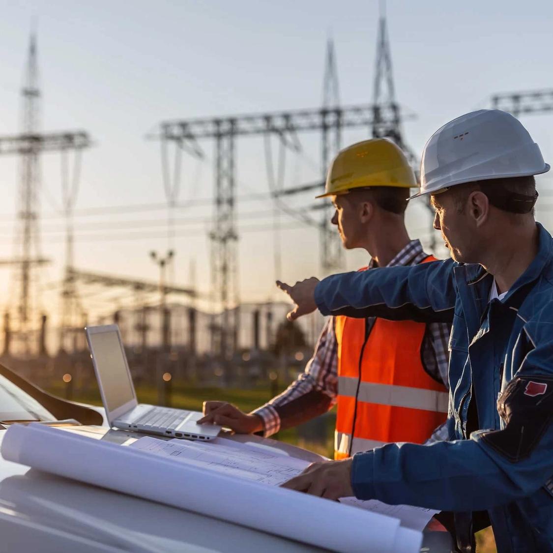 Blue collar worker points towards sun setting over power distribution center with white collar worker looking the same direction.