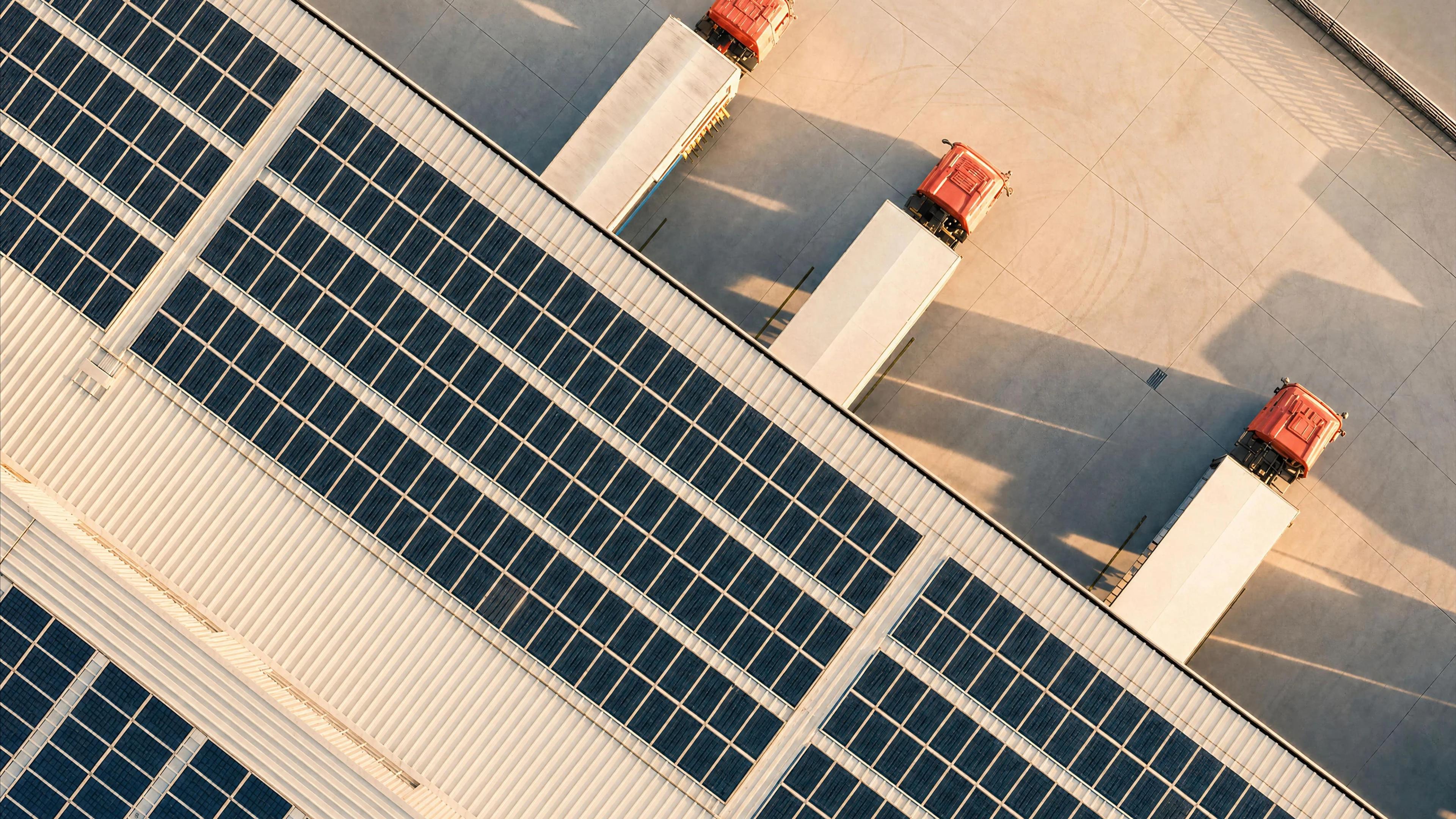 Warehouse with solar panels on the roof and three trucks.