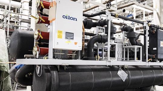 Industrial refrigeration or heat pump system with large black insulated pipes and an Oilon control unit installed in a mechanical plant room.